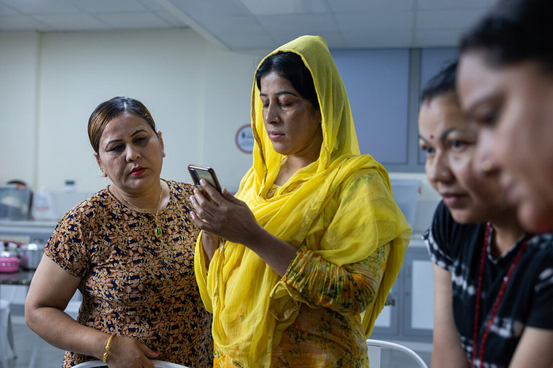Three women are looking at the NOW Money digital banking app, deep in concentration.